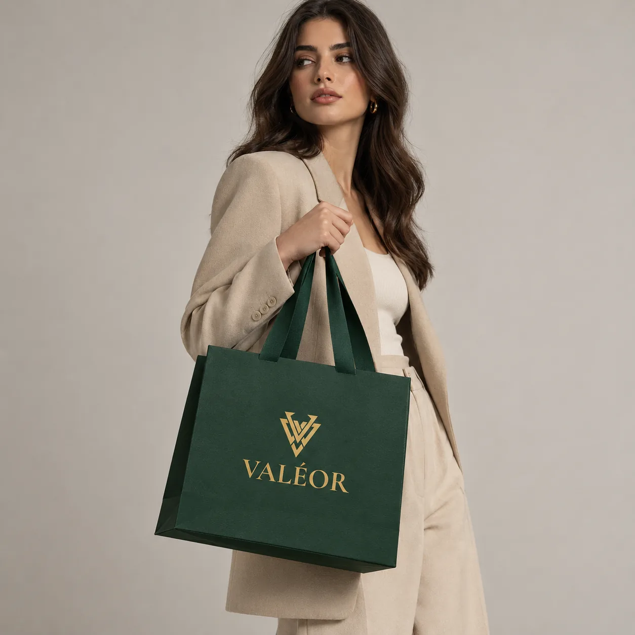 A woman in a beige wool suit carrying the green VALÉOR shopping bag with its gold logo